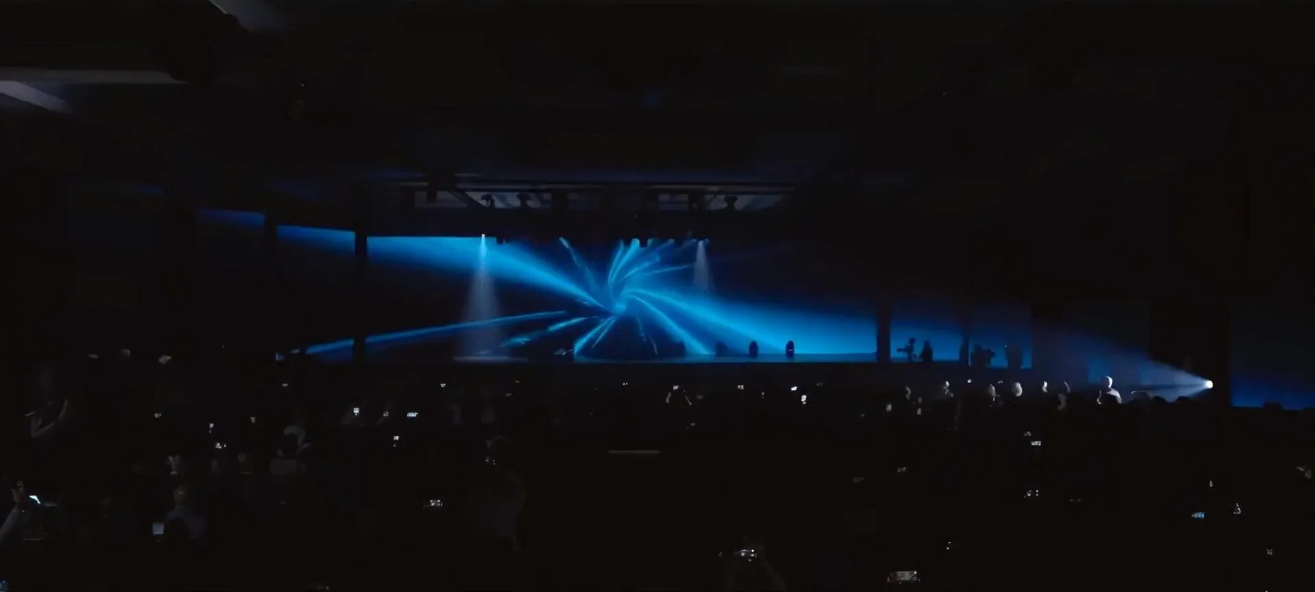 Blue light beams fan out from the stage over the darkened room