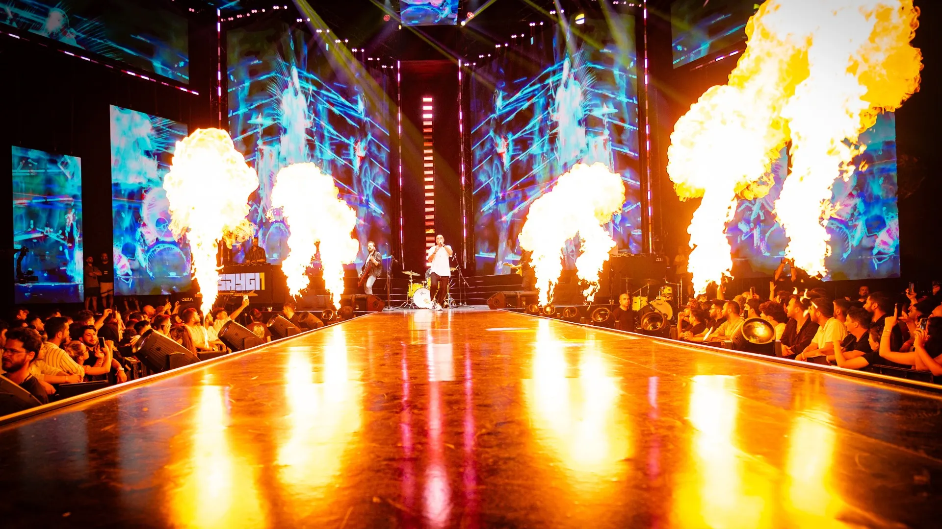 Flame jets line both sides of the runway between screens of shifting imagery
