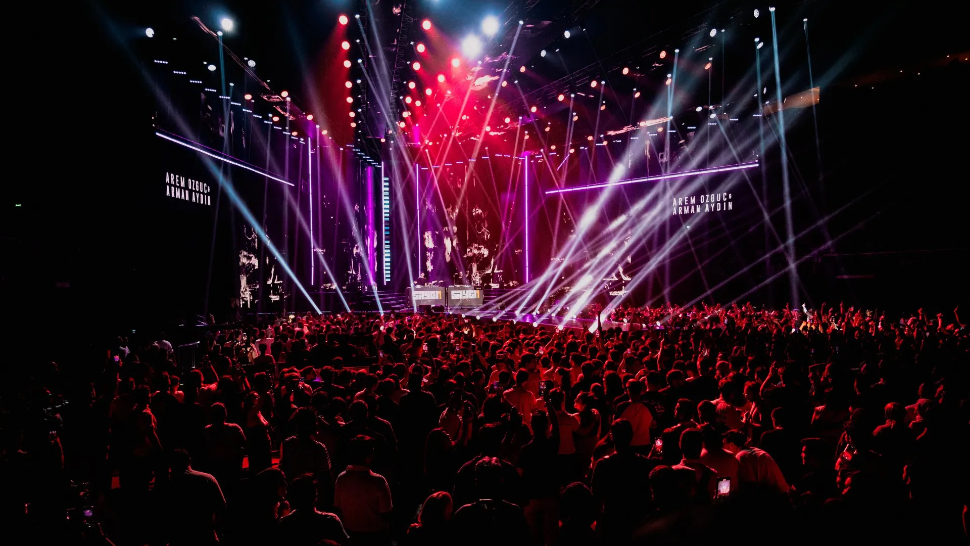 The arena crowd under a red and violet light show, the stage glowing at the far end
