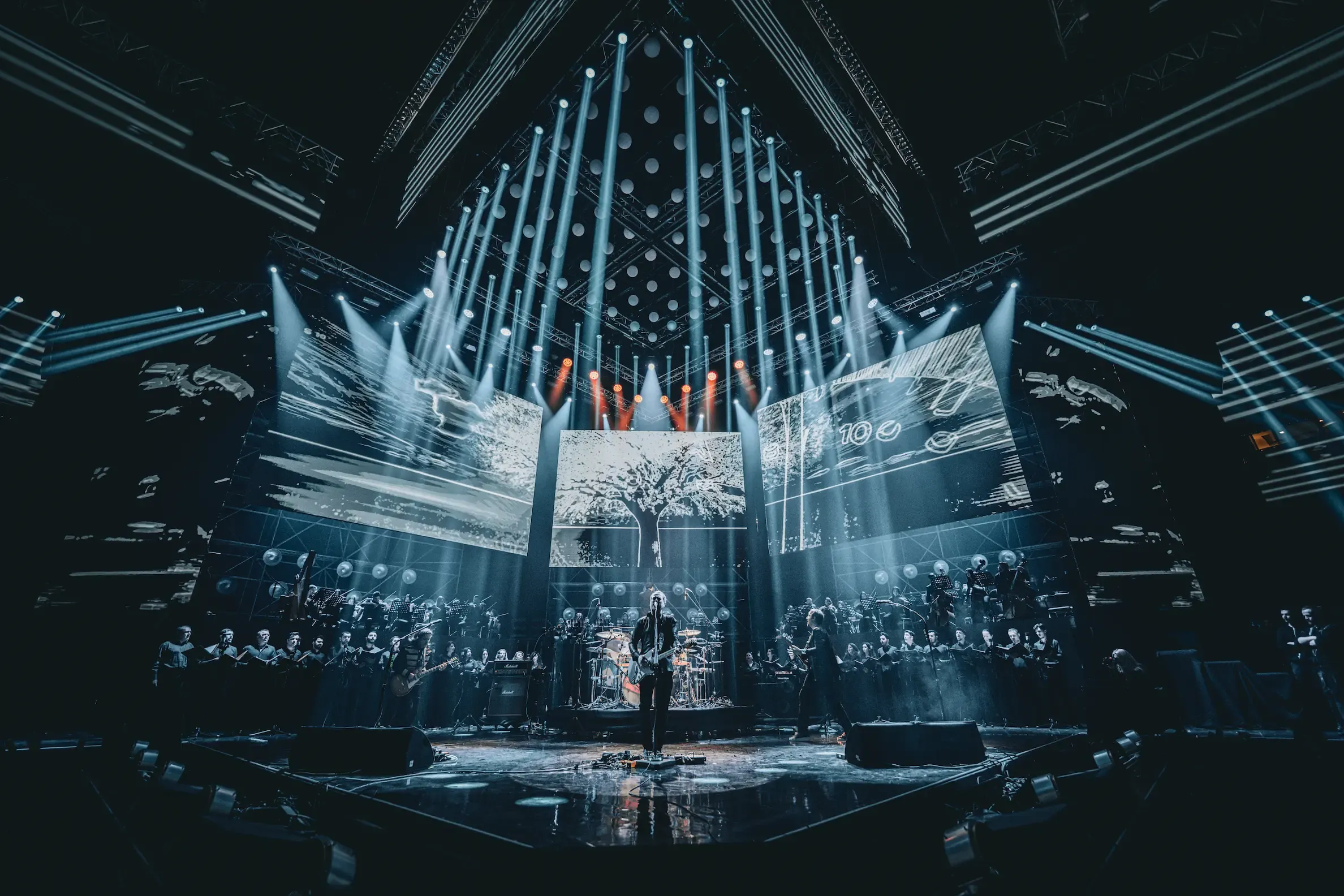 The orchestra and choir revealed on tiered risers under a fan of white light, the band at centre stage