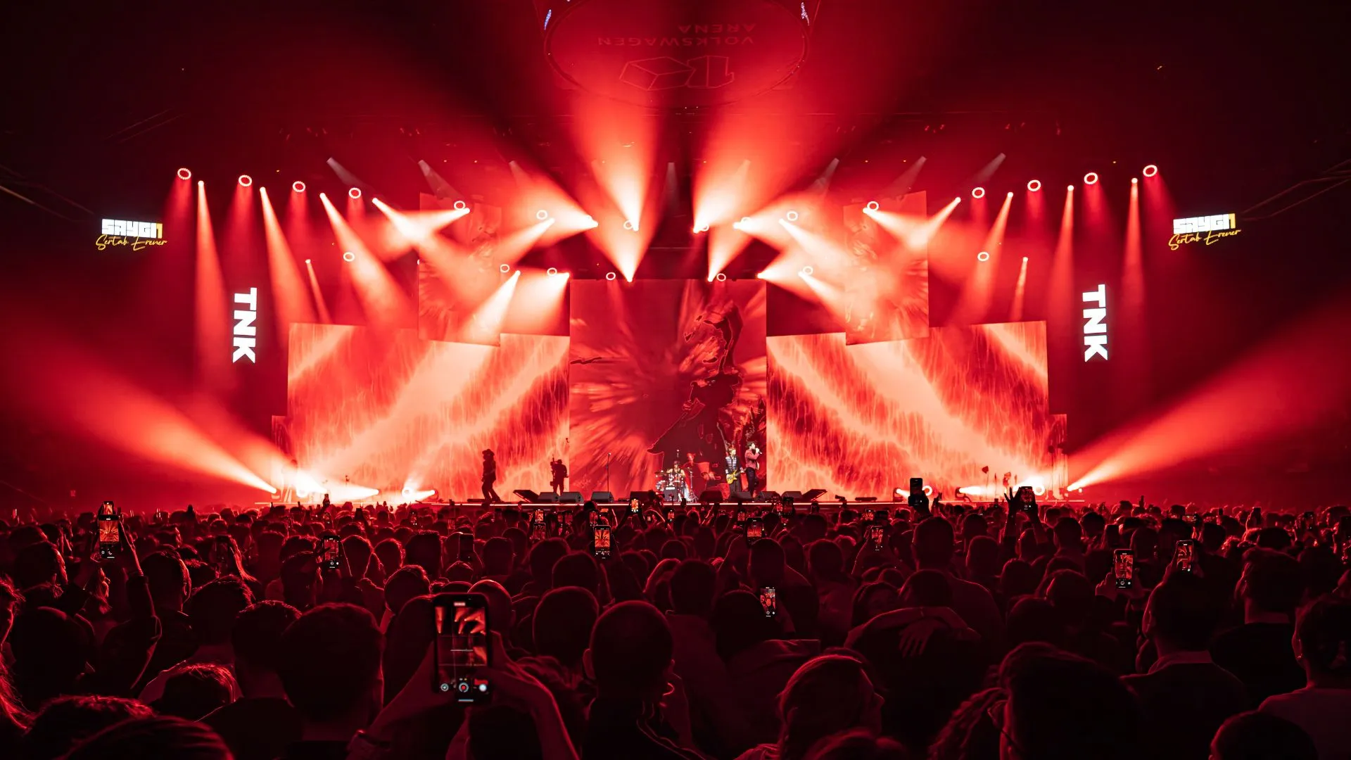 The stage blazing red, beams converging over a crowd with raised hands