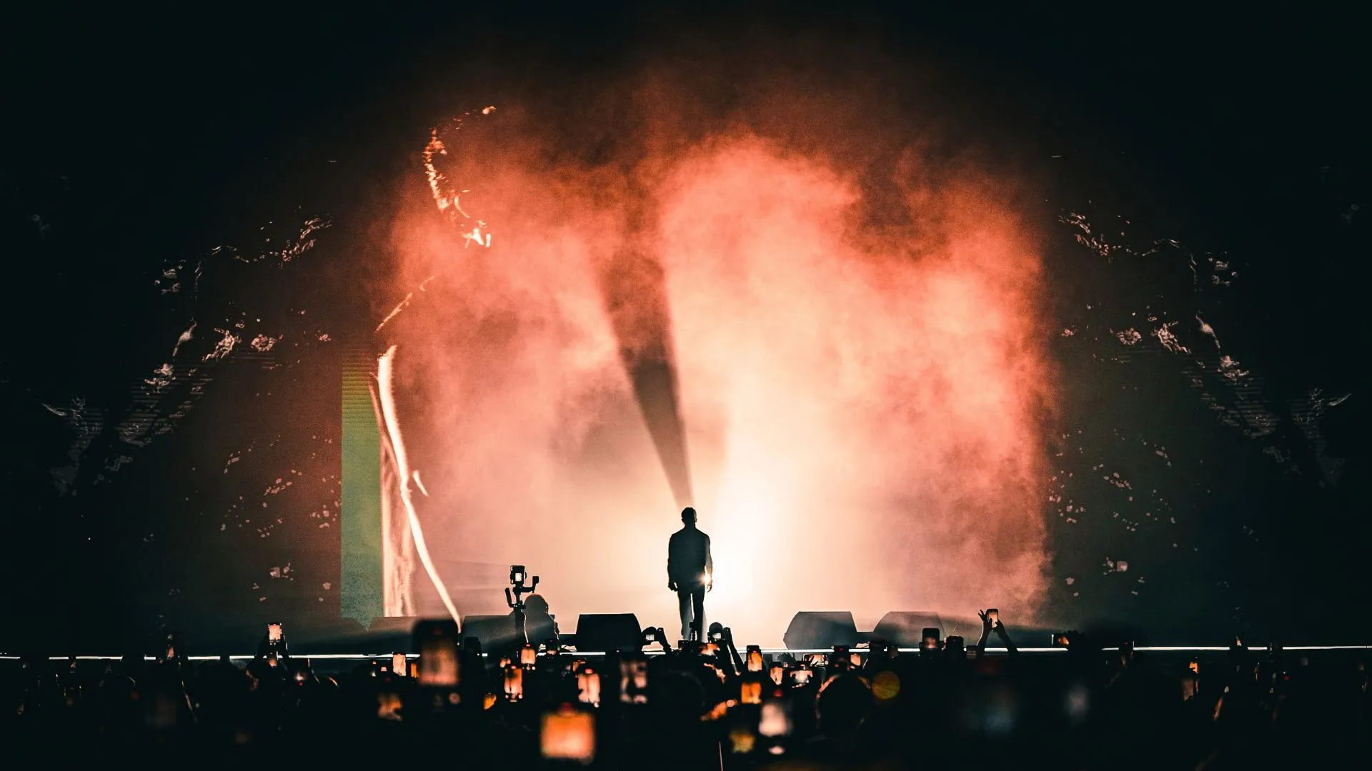A lone performer in silhouette against a wall of pink haze and light