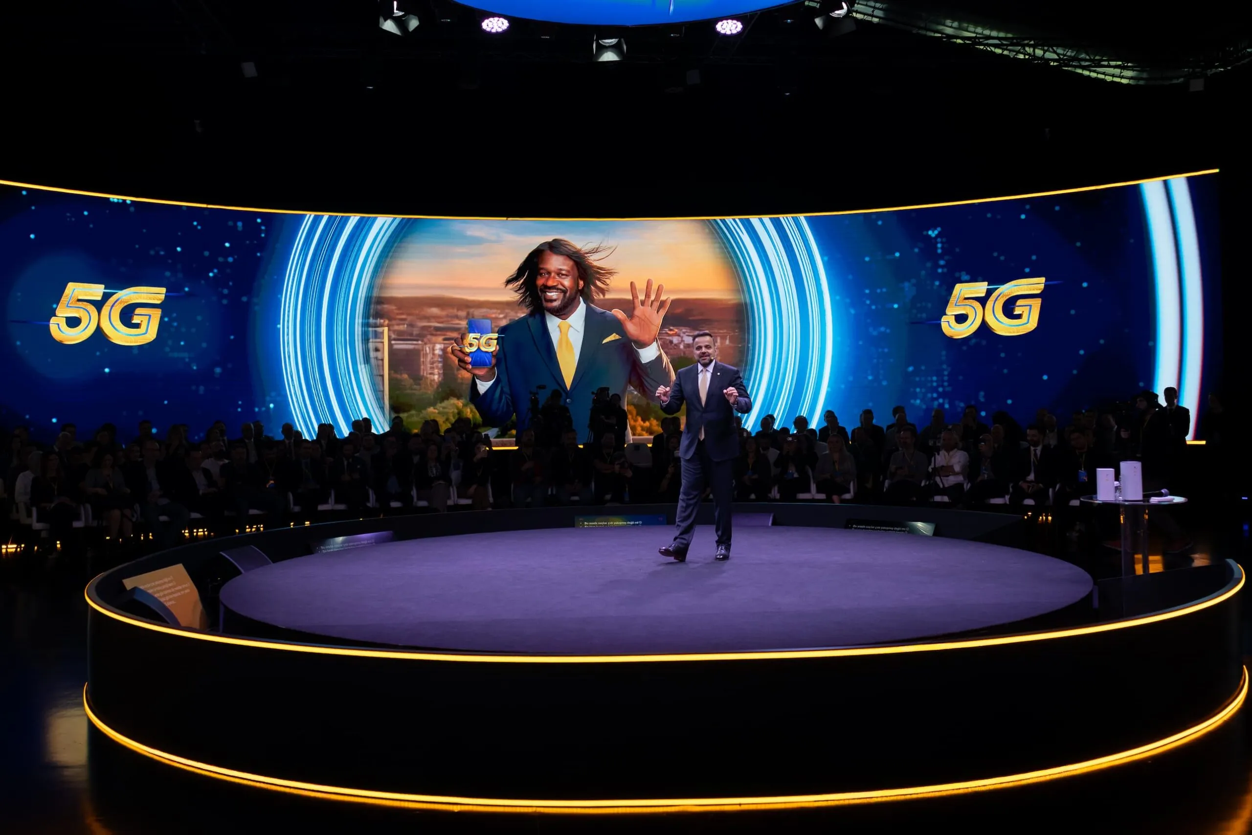 A Turkcell executive on the circular stage, Shaquille O'Neal on the curved LED wall behind him, the press seated in a ring around the podium