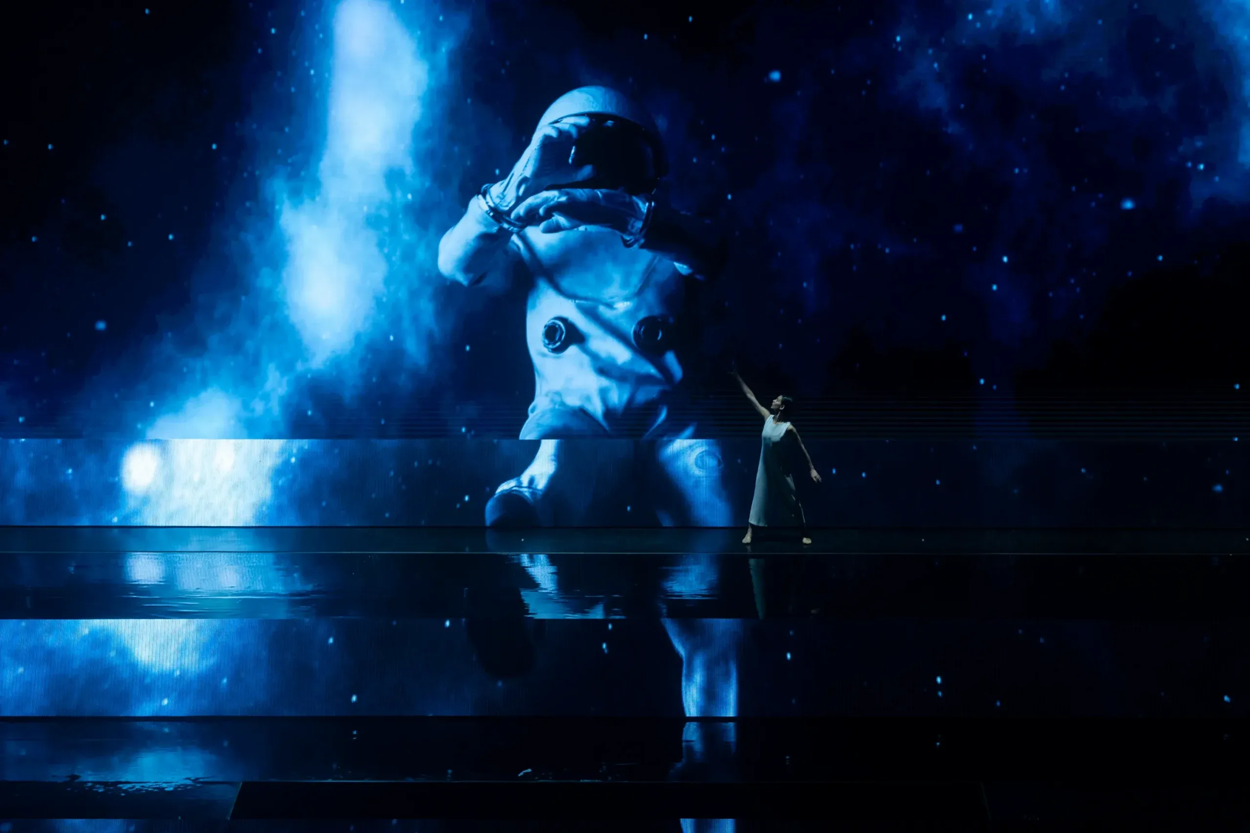 A performer beside a giant projected astronaut floating in blue haze