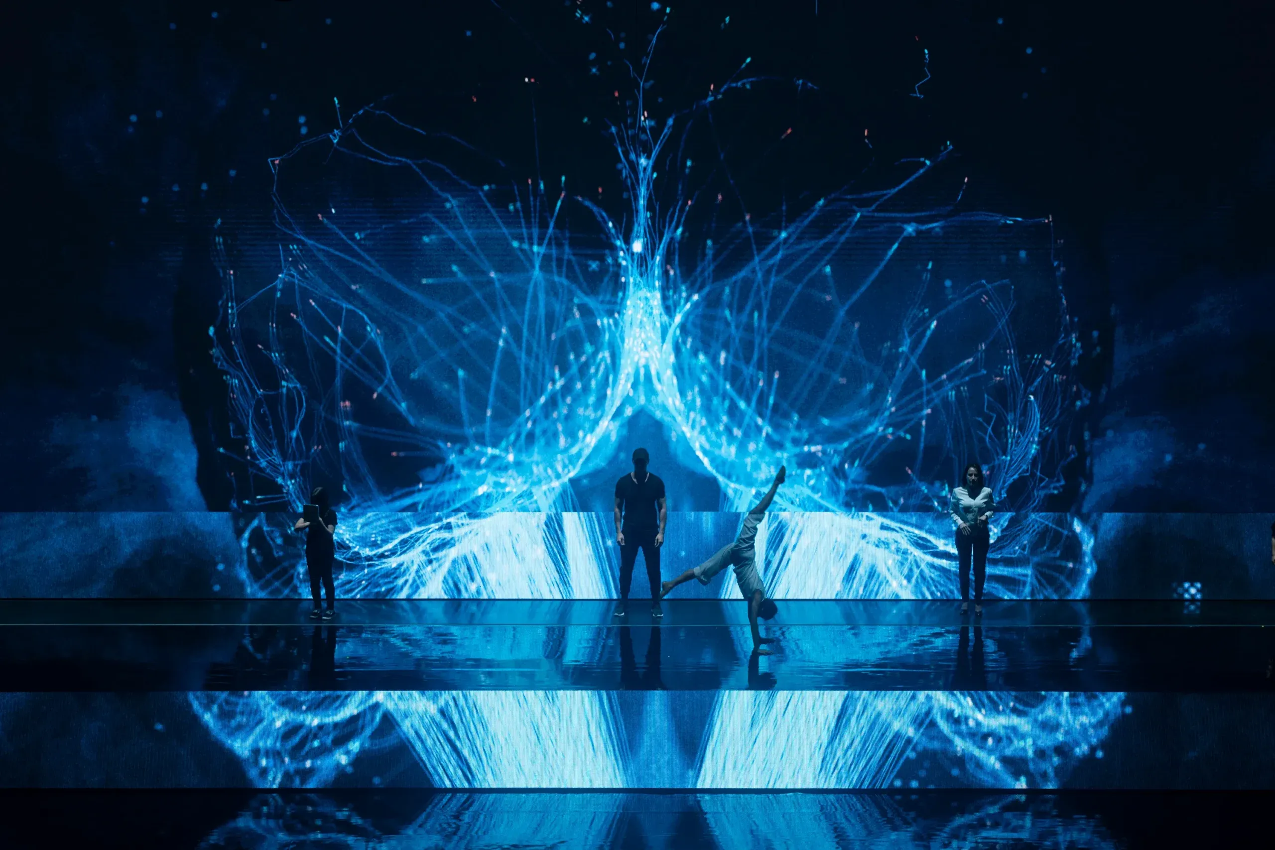 Dancers in silhouette inside a glowing blue network of light