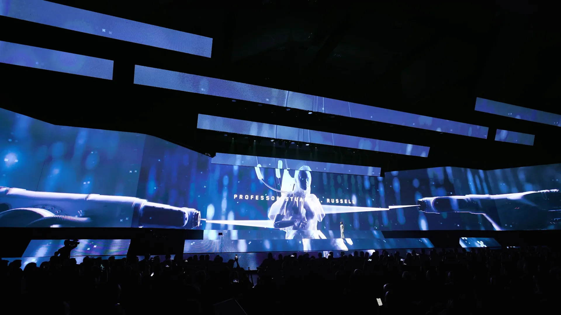 The three-tier stage during the opening, a performer crossing beneath a projected astronaut