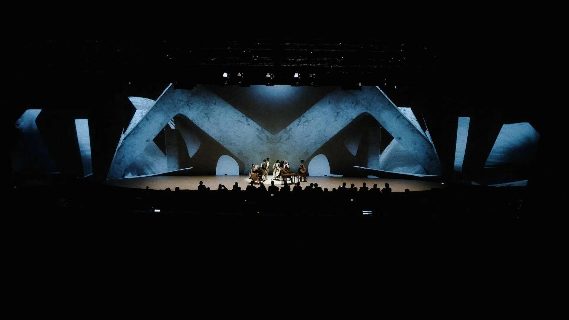 Sculptural stage architecture lit blue, rising above the musicians, the congress audience in silhouette
